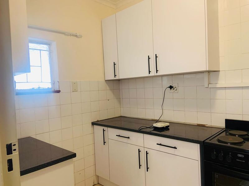 A functional kitchen featuring white cabinetry, dark stone countertops, a tiled backsplash, and a built-in oven with an electric hob.