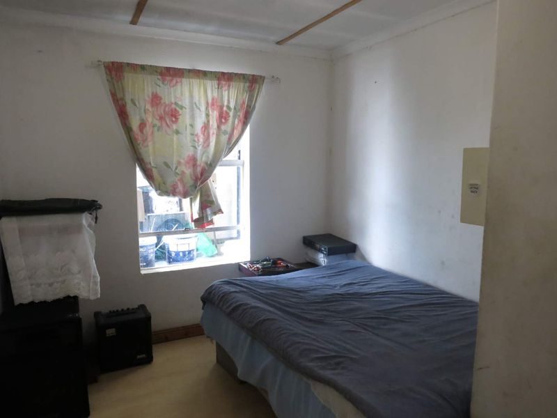 A compact bedroom featuring a single window with natural light, requiring cosmetic updates to the walls and ceiling finishes.