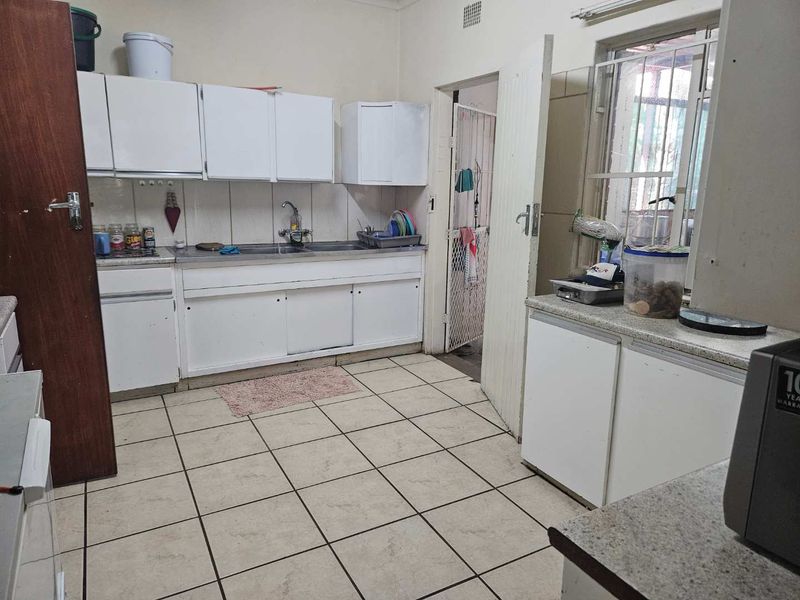 A functional kitchen featuring white built-in cabinetry, a stainless steel sink, and tiled flooring, offering potential for modernization and cosmetic updates.