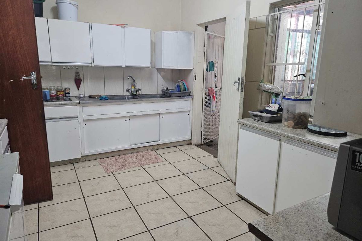 A functional kitchen featuring white built-in cabinetry, a stainless steel sink, and tiled flooring, offering potential for modernization and cosmetic updates.