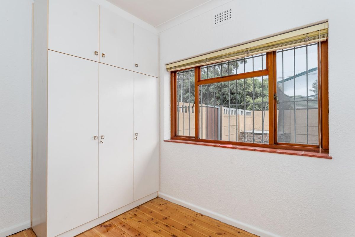 A bedroom featuring built-in floor-to-ceiling cabinetry, polished timber flooring, and a window with security bars overlooking the rear yard.