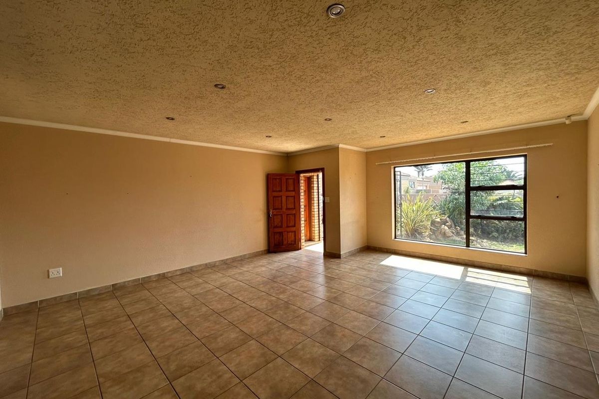 A spacious, empty living room featuring tiled flooring, recessed downlighting, and a large window providing natural light and garden views.