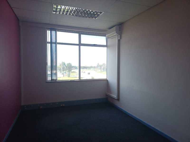 A vacant office space featuring a large window, suspended ceiling with recessed lighting, split-system air conditioning, and carpeted flooring.