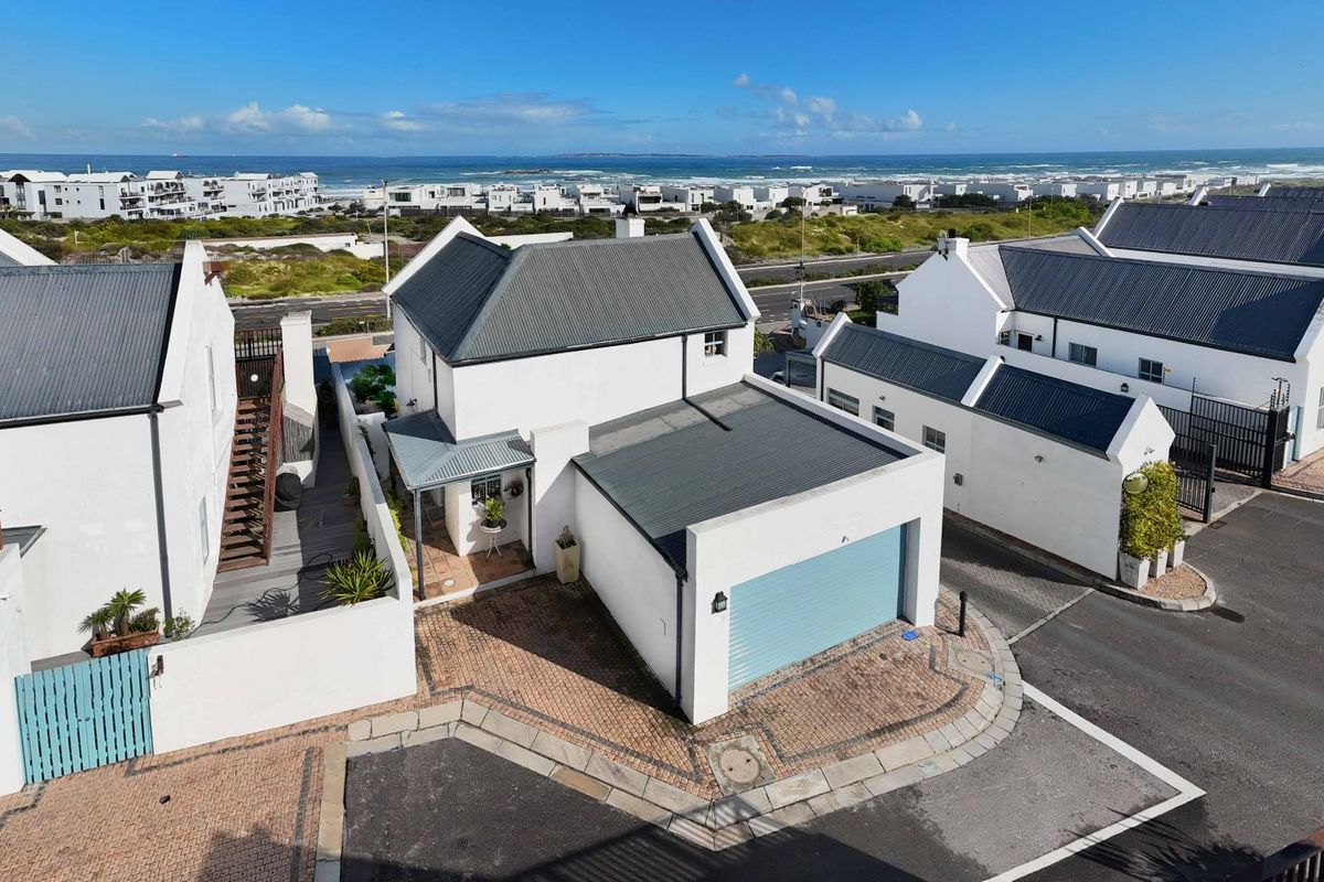 Aerial view of a coastal townhouse featuring a corrugated metal roof, attached garage, and paved driveway, situated in a well-maintained residential estate.