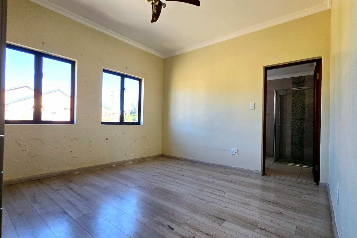 An empty bedroom featuring wood-look laminate flooring, a ceiling fan, and an en-suite bathroom with a glass-enclosed shower.