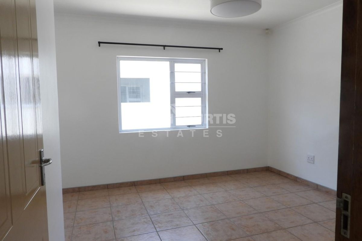 A clean, empty bedroom featuring neutral tiled flooring, a large aluminium window, and a simple flush mount ceiling light fixture.