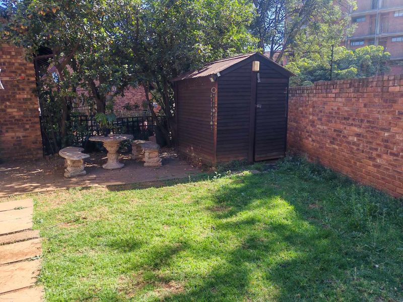 A private rear garden featuring a brick boundary wall, a paved patio area, and a wooden storage shed set within a lawned space.