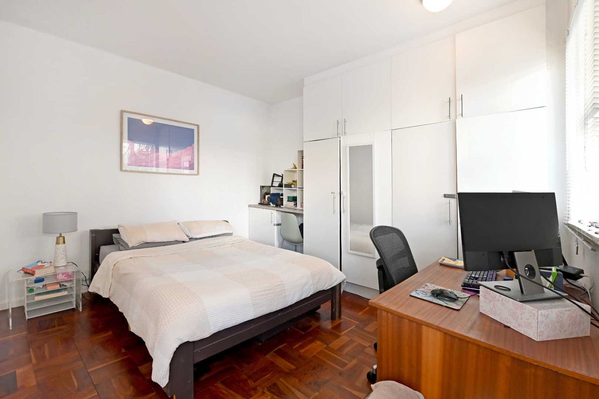 A well-lit bedroom featuring polished parquet flooring and extensive built-in white cabinetry providing ample storage space.