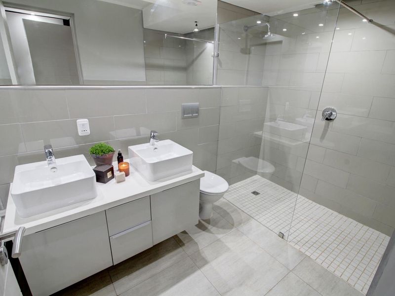 Modern bathroom featuring a double vanity with vessel sinks, a spacious walk-in shower with a glass screen, and contemporary wall-mounted toilet.