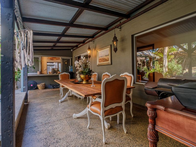 A covered outdoor patio area featuring exposed beam ceilings, corrugated roofing, and durable aggregate concrete flooring, ideal for alfresco dining and entertaining.