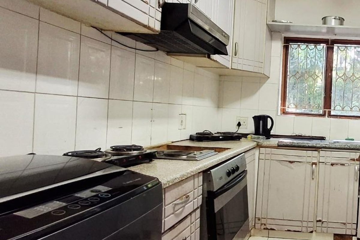 A functional kitchen featuring built-in cabinetry, an integrated oven, and extractor fan, with tiled surfaces throughout. The space shows signs of wear and dated finishes.