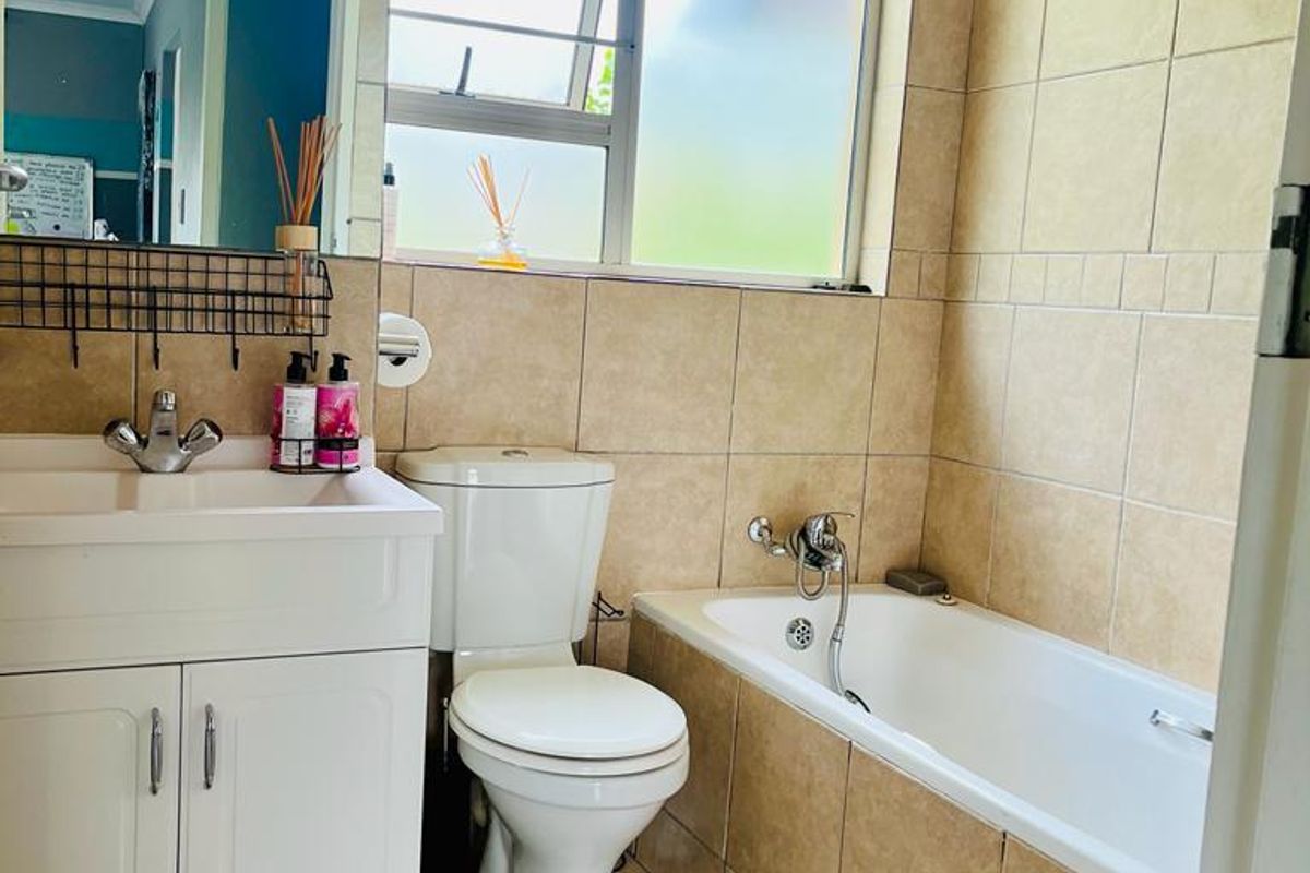 A functional bathroom featuring a built-in vanity, a standard toilet, and a tiled bathtub with shower mixer.
