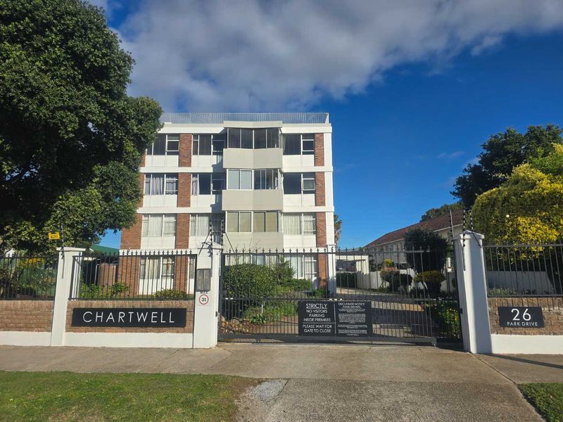 Front elevation of Chartwell apartment complex featuring a secure gated entrance, brick boundary walls, and multi-story residential units with balconies.