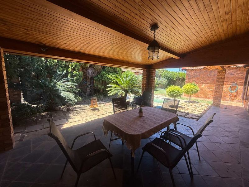 A covered patio area featuring a timber-clad ceiling, brick support pillars, and stone tile flooring, overlooking a landscaped garden.