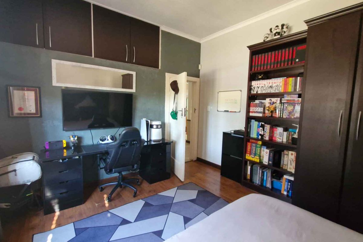A bedroom featuring built-in overhead cabinetry, laminate flooring, and a neutral wall finish, currently utilized as a home office and study space.