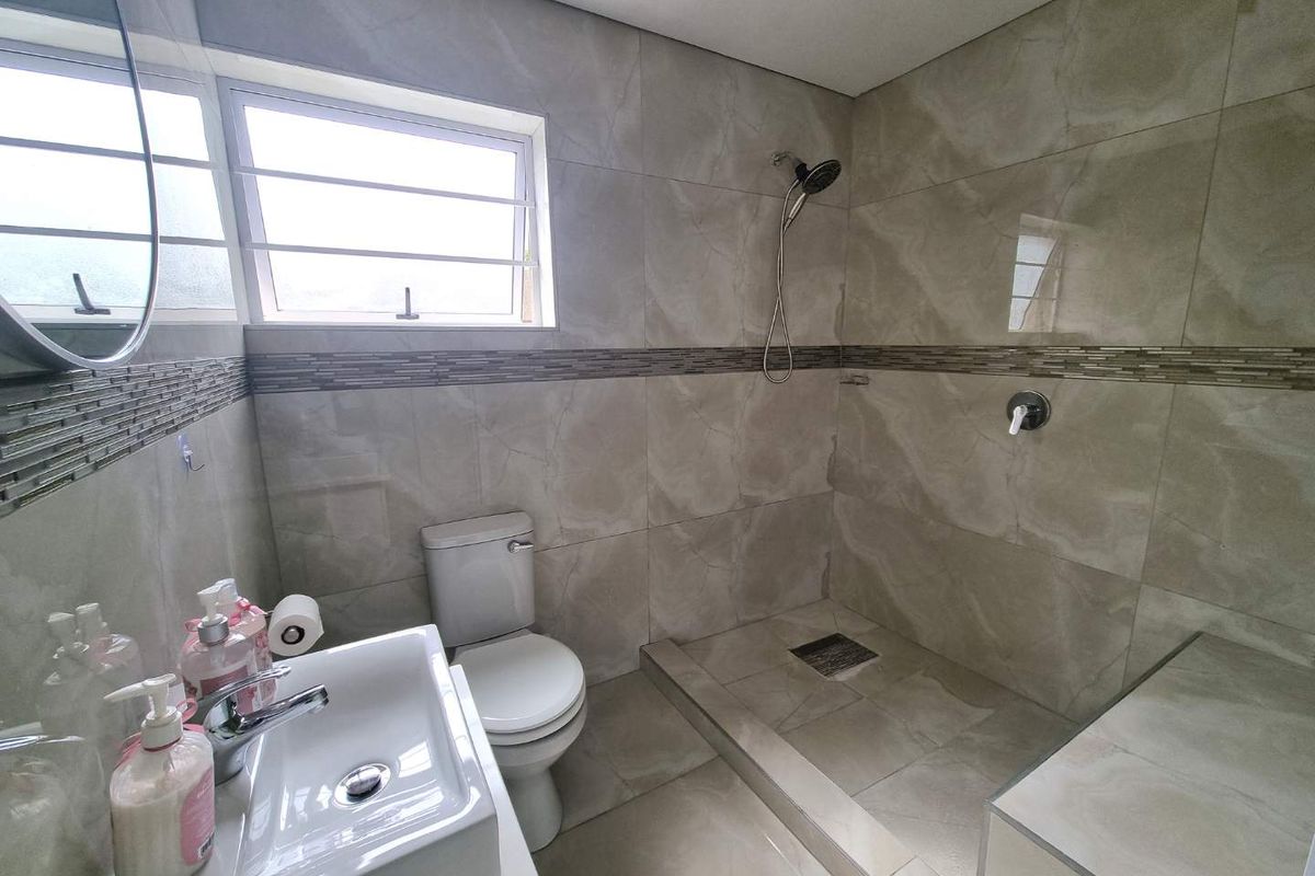 Modern bathroom featuring floor-to-ceiling neutral tiling, a walk-in shower with a rainfall showerhead, a contemporary basin, and a toilet.