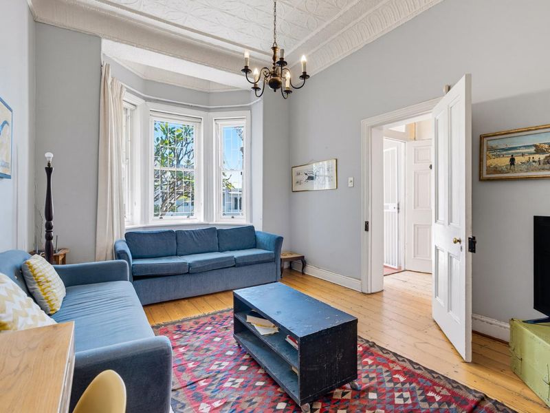 A character-filled living room featuring a classic bay window, original timber flooring, and an ornate ceiling with period detailing.
