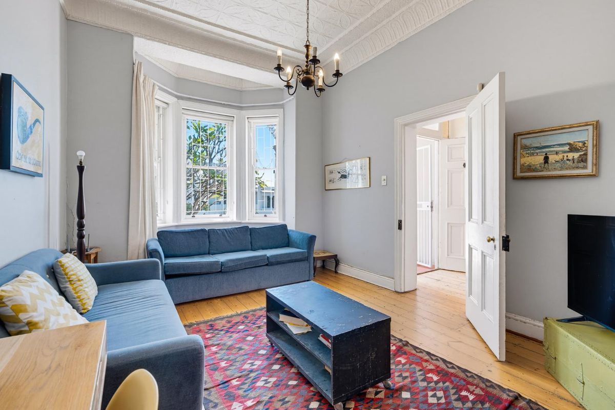 A character-filled living room featuring a classic bay window, original timber flooring, and an ornate ceiling with period detailing.