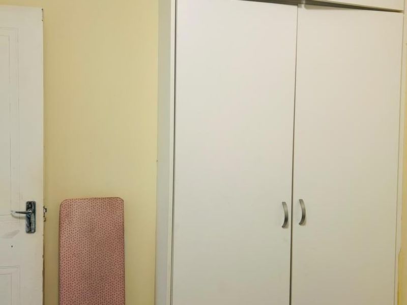 A bedroom interior featuring a white built-in wardrobe with integrated overhead storage cupboards.