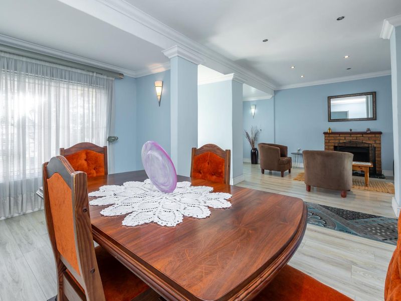Spacious open-plan living and dining area featuring a classic brick fireplace, crown molding, and light-toned laminate flooring throughout.
