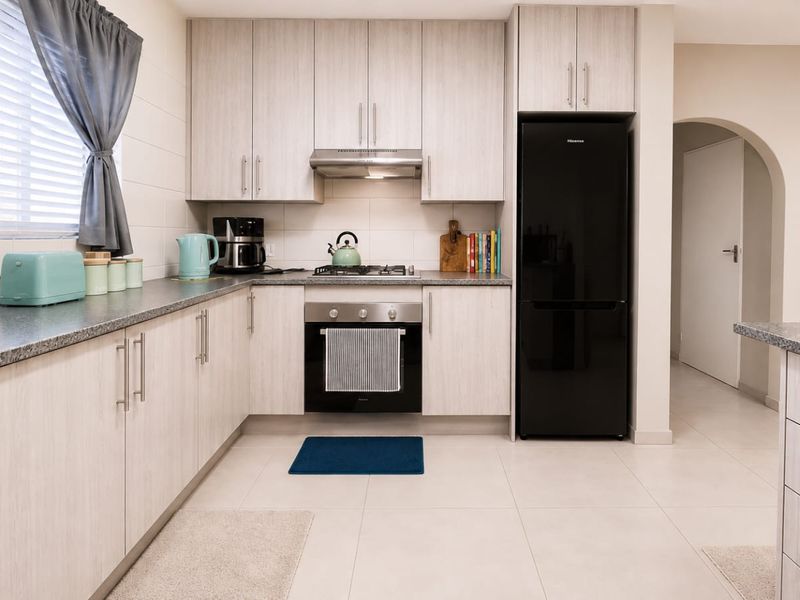 A well-maintained kitchen featuring light wood-grain cabinetry, granite-look countertops, built-in oven with gas hob, and neutral floor tiles.