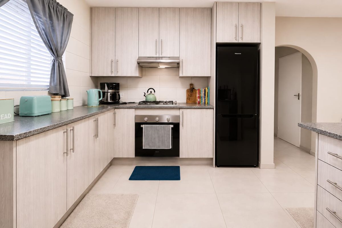 A well-maintained kitchen featuring light wood-grain cabinetry, granite-look countertops, built-in oven with gas hob, and neutral floor tiles.