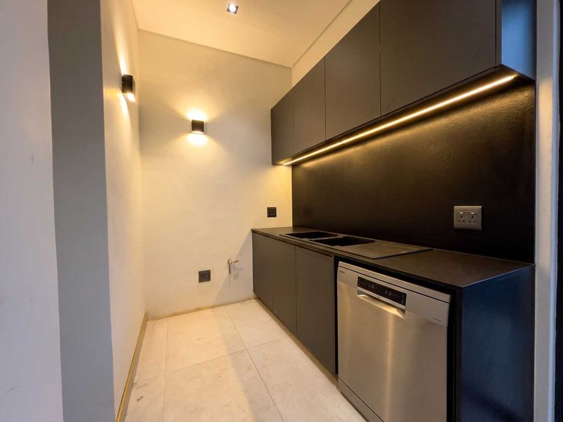 A modern, minimalist scullery featuring sleek dark cabinetry, integrated sink, under-cabinet LED lighting, and tiled flooring, providing a clean and functional utility space.