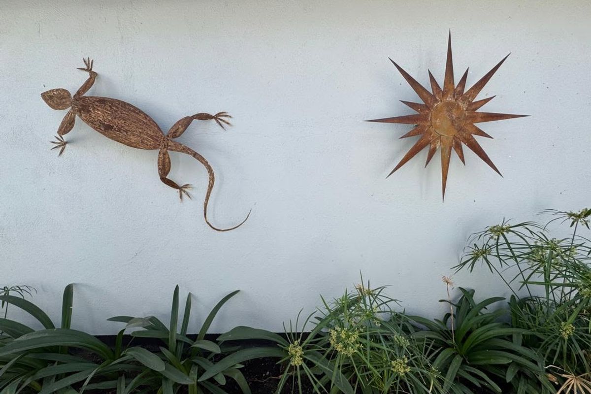 A close-up view of a plastered exterior wall featuring decorative metal wall art and a landscaped garden bed at the base.
