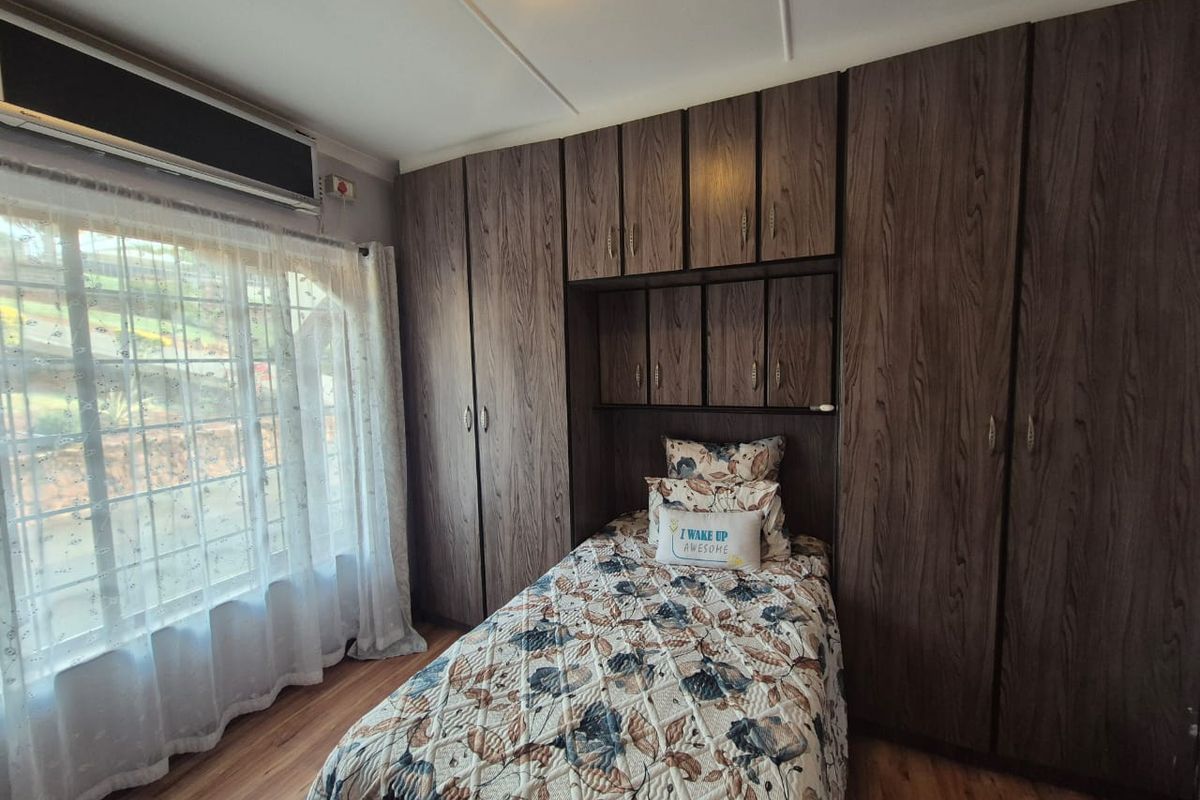 A bedroom featuring extensive built-in wooden cupboards, laminate flooring, and an integrated air conditioning unit.