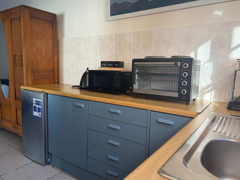 A compact kitchen area featuring blue cabinetry, a light wood-look laminate countertop, a stainless steel sink, and neutral tiled splashbacks.