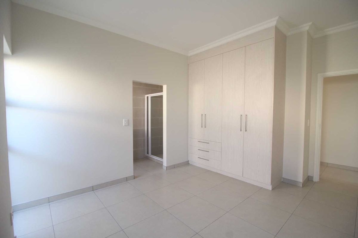 A bright, modern bedroom featuring neutral tiled flooring, built-in cupboards, and direct access to an en-suite bathroom.