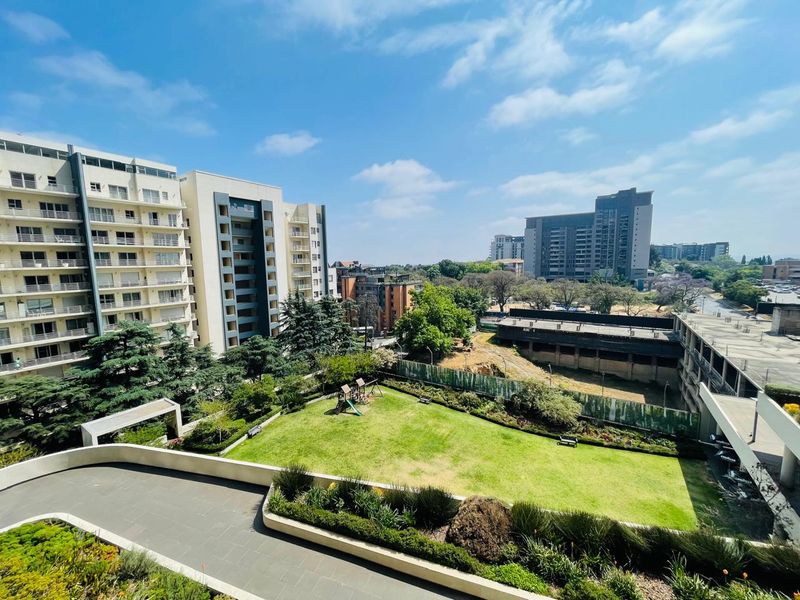 Elevated view overlooking a well-maintained communal garden area with paved pathways and surrounding apartment buildings.