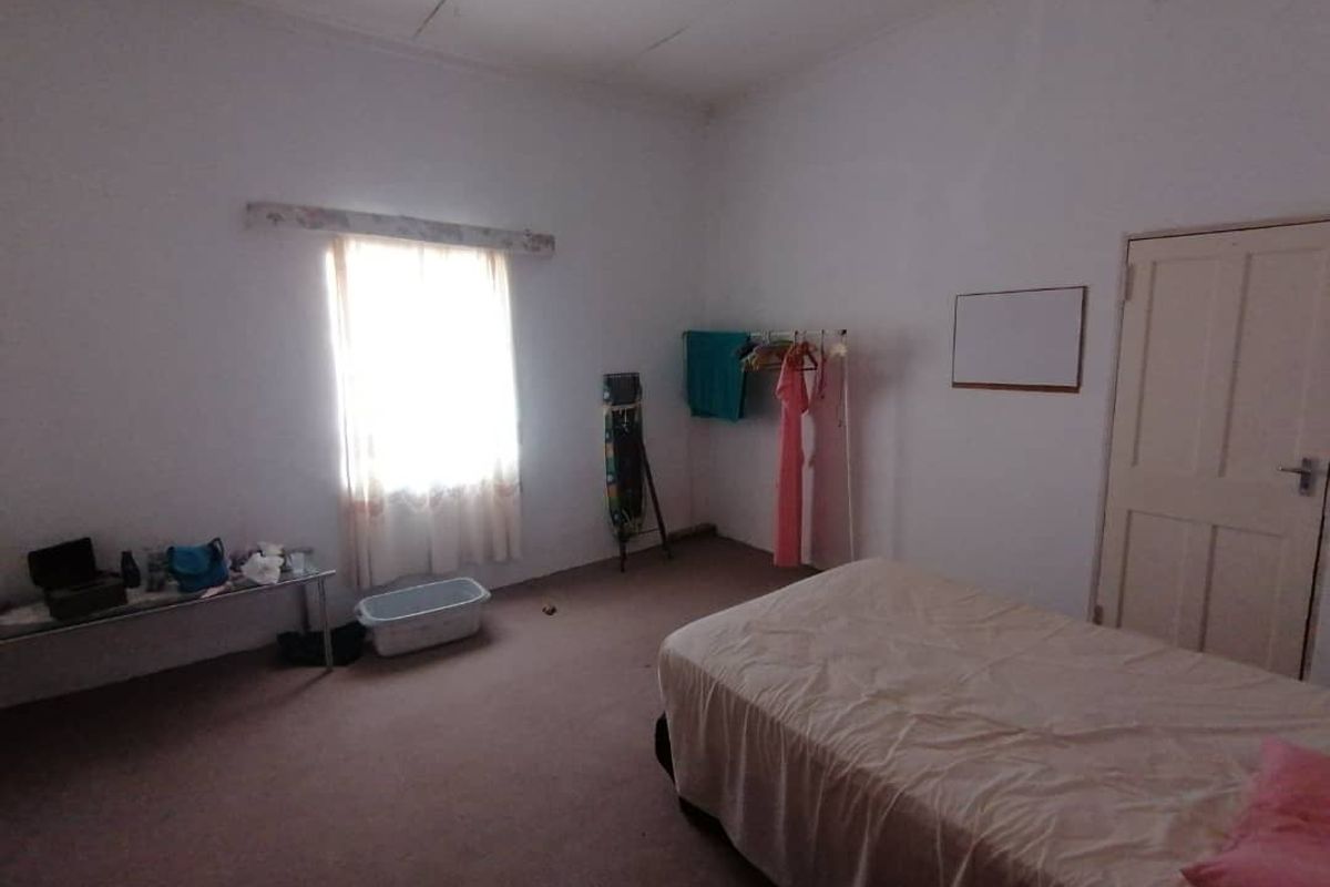 A simple bedroom featuring carpeted flooring, a single window with natural light, and standard interior door access.