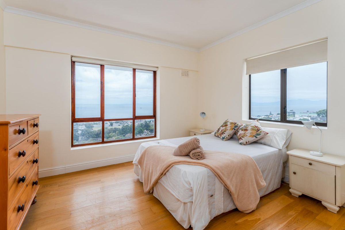 A bright bedroom featuring timber flooring, large windows with scenic coastal views, and neutral wall finishes.