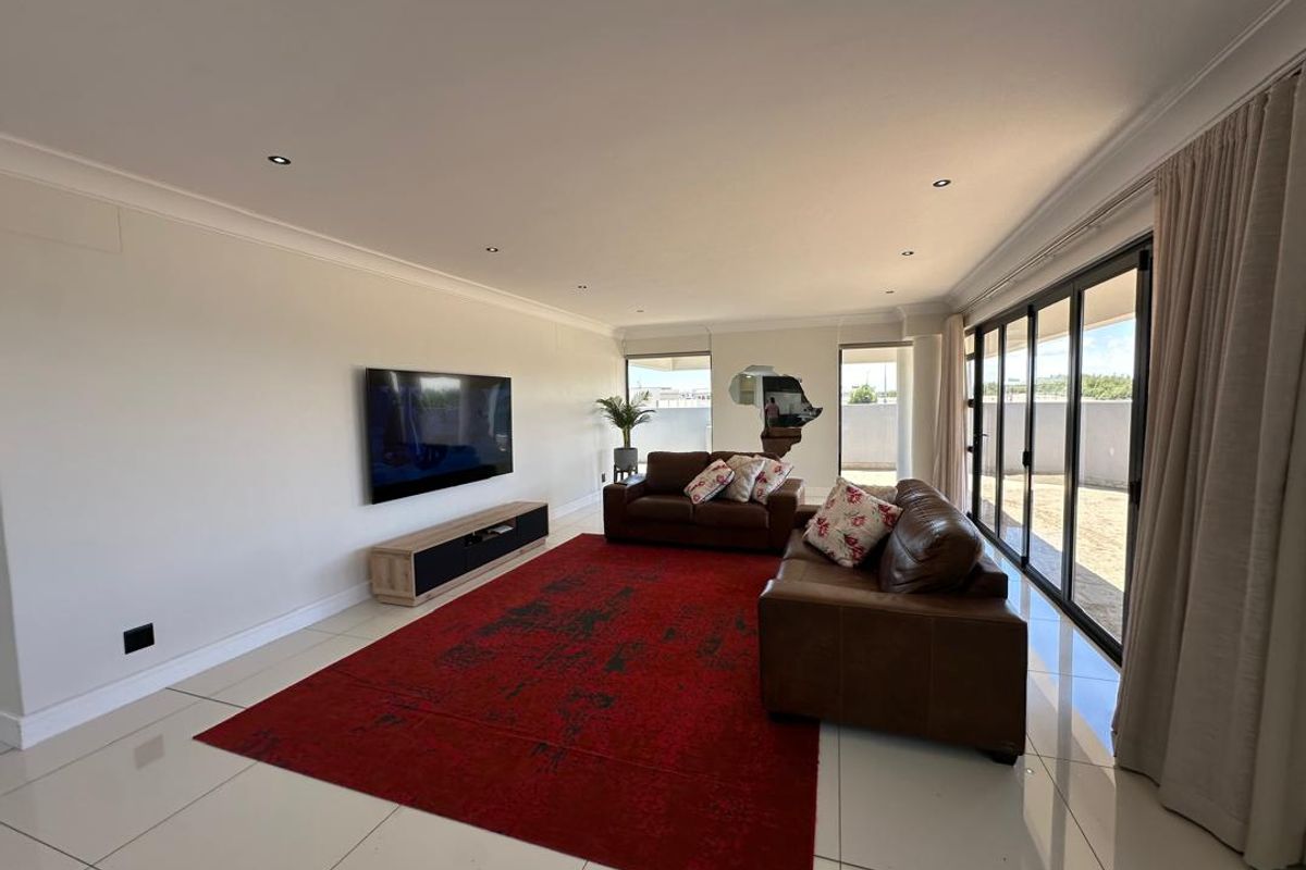 Spacious living room featuring large format floor tiles, recessed downlighting, and expansive sliding glass doors providing seamless access to the outdoor area.