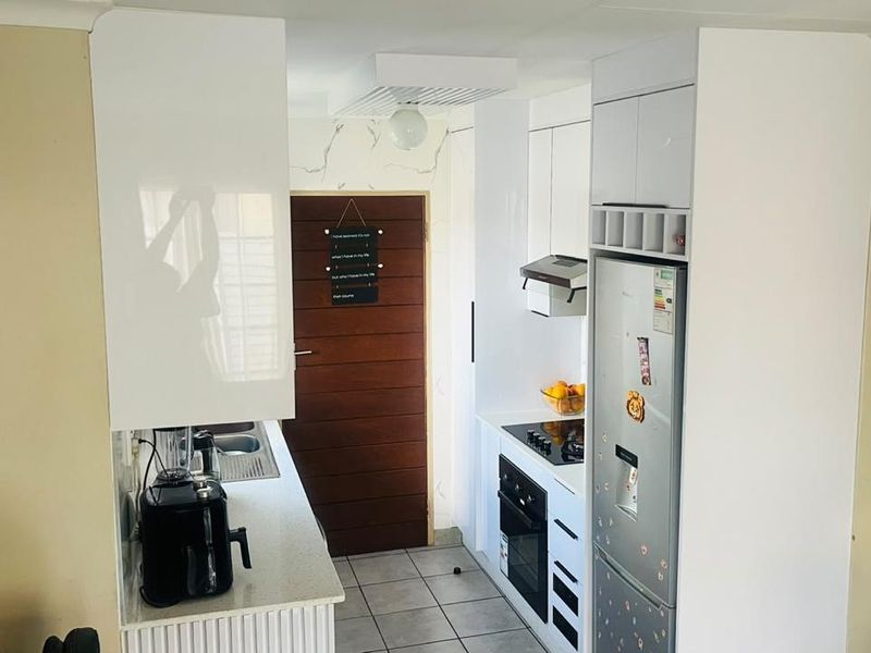 A compact, modern kitchen featuring white high-gloss cabinetry, stone countertops, integrated appliances including an oven and hob, and tiled flooring.
