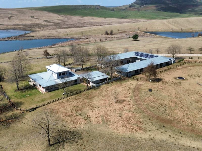 Aerial view of a large farm property featuring multiple buildings with metal roofing, solar panels, and expansive surrounding landscape with dams.