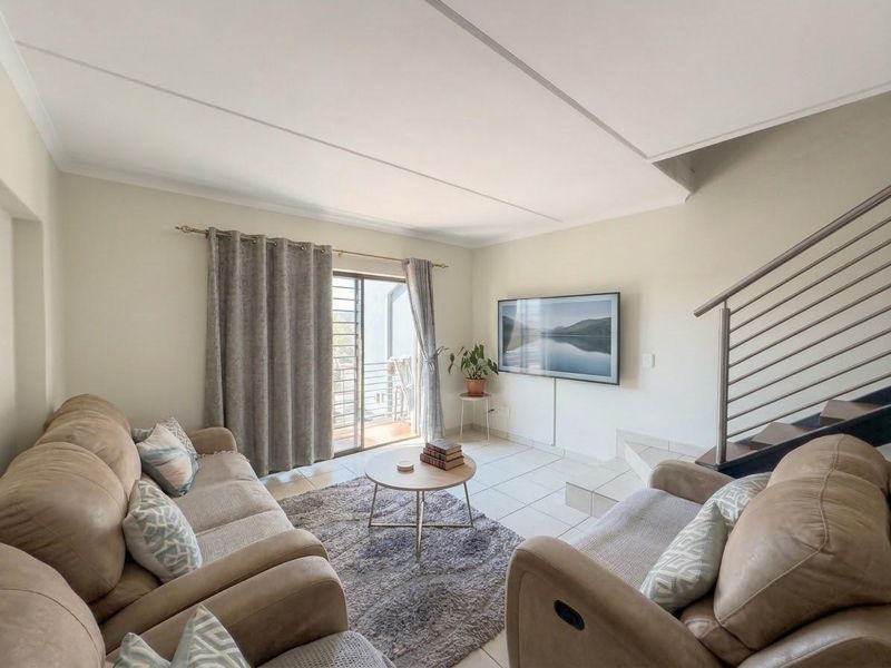 A bright living room featuring tiled flooring, a staircase with a modern metal railing, and a sliding glass door leading to an outdoor area.