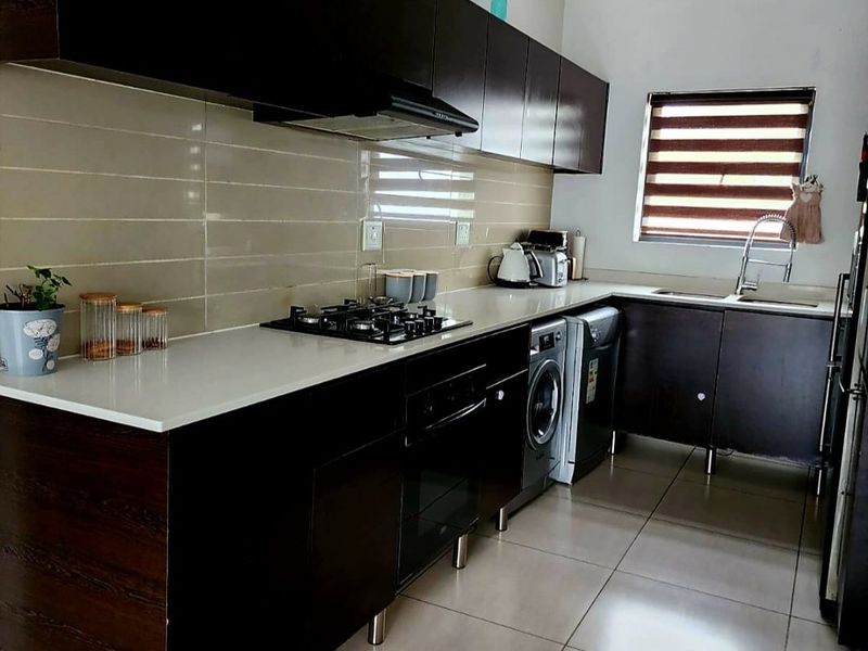 Modern kitchen featuring dark wood cabinetry, stone countertops, integrated gas hob, built-in oven, and tiled backsplash with neutral floor tiles.