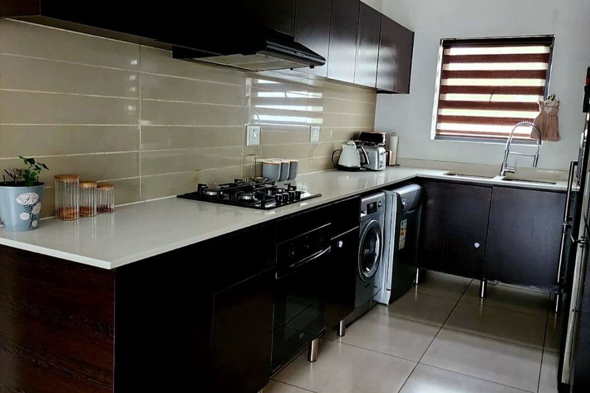 Modern kitchen featuring dark wood cabinetry, stone countertops, integrated gas hob, built-in oven, and tiled backsplash with neutral floor tiles.