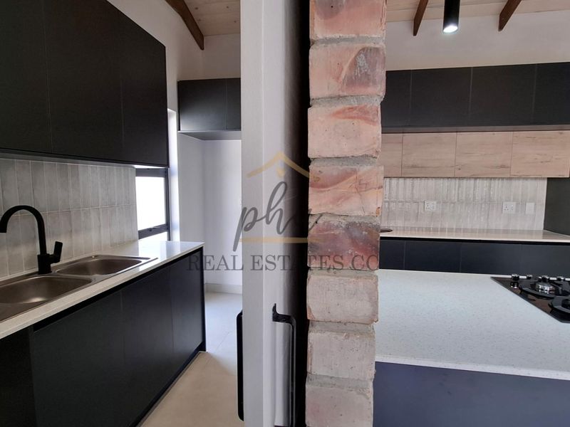 Modern kitchen featuring dark cabinetry, stone countertops, a gas hob, built-in oven, and unique exposed brick and timber ceiling architectural details.
