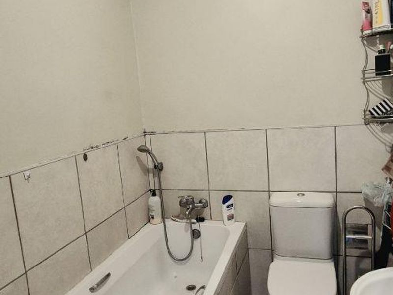 A functional bathroom featuring a bathtub with handheld shower, toilet, and pedestal basin, finished with ceramic tiling throughout.