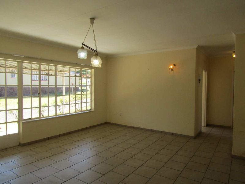 A spacious, empty living area featuring neutral tiled flooring, large grid-pattern windows providing natural light, and classic coved ceilings.