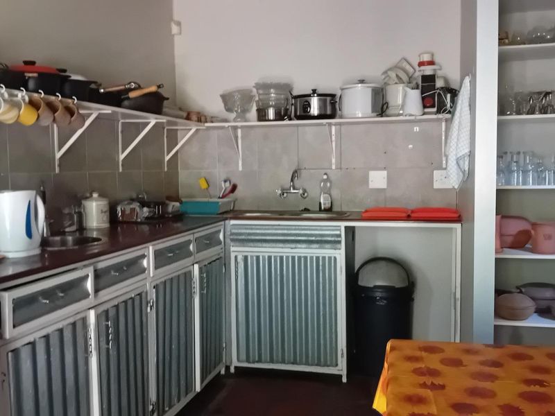 A functional kitchen featuring corrugated metal cabinetry, open shelving, and a tiled backsplash, offering a rustic industrial aesthetic with ample storage space.