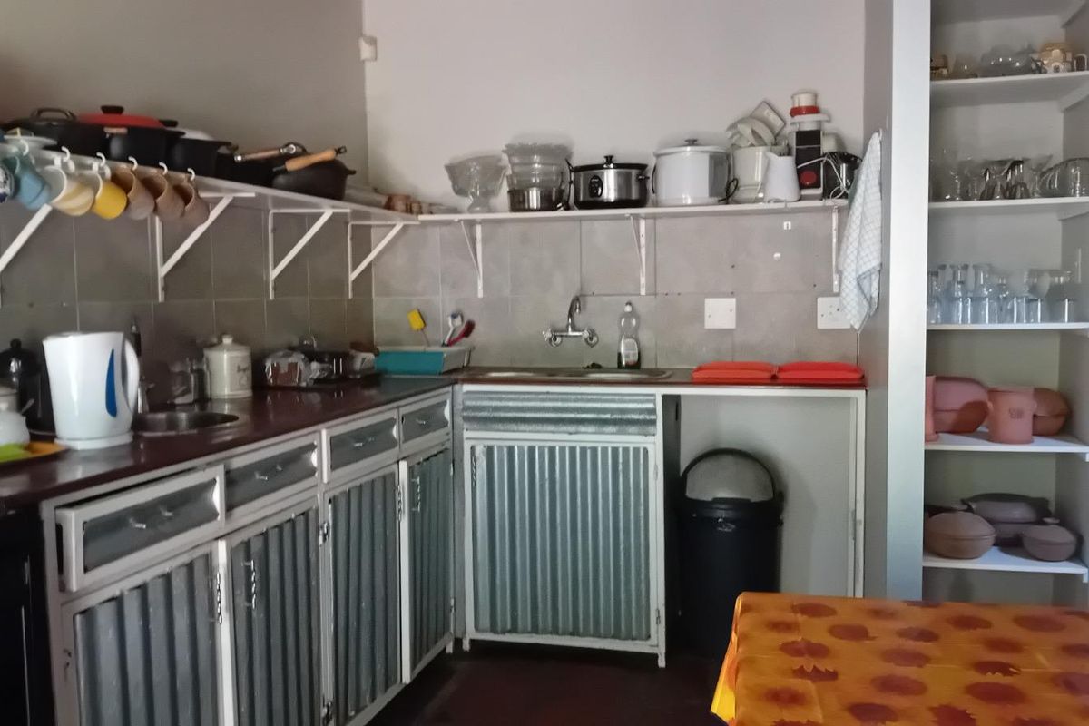A functional kitchen featuring corrugated metal cabinetry, open shelving, and a tiled backsplash, offering a rustic industrial aesthetic with ample storage space.