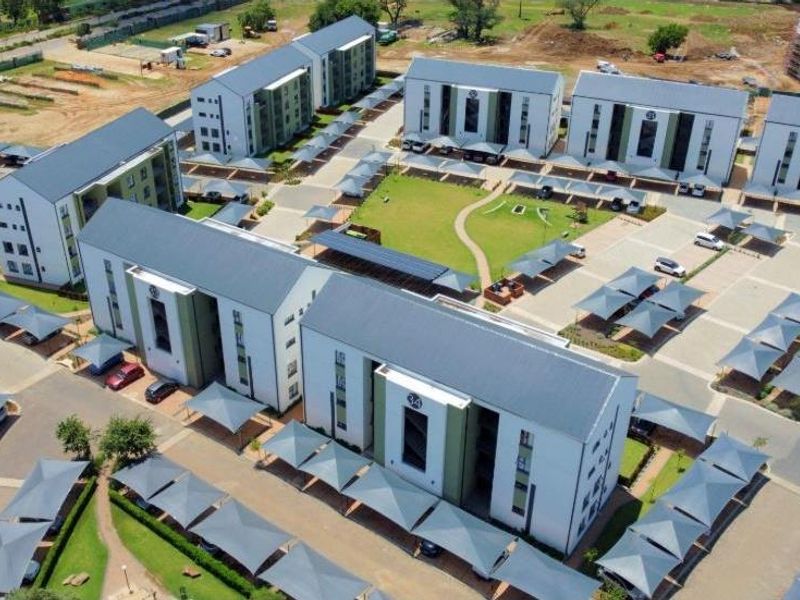 Aerial view of a modern apartment complex featuring multiple residential blocks, extensive paved parking with carports, and well-maintained communal garden areas.