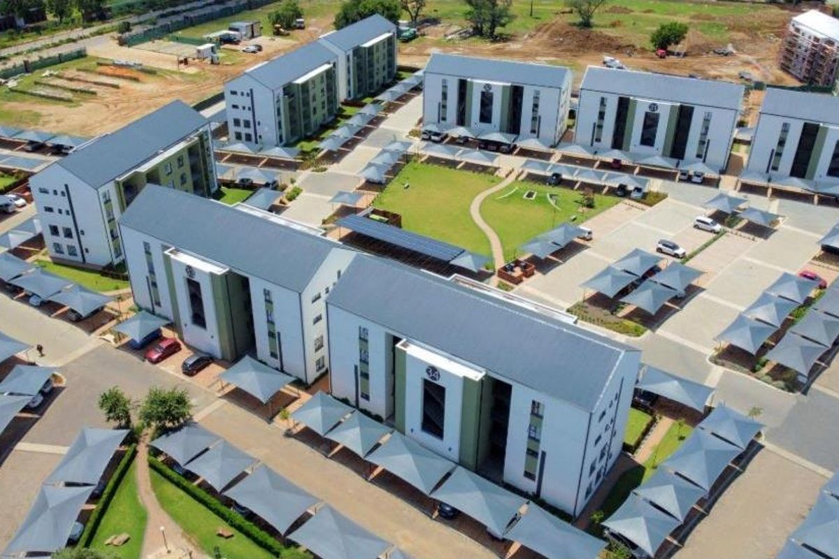 Aerial view of a modern apartment complex featuring multiple residential blocks, extensive paved parking with carports, and well-maintained communal garden areas.