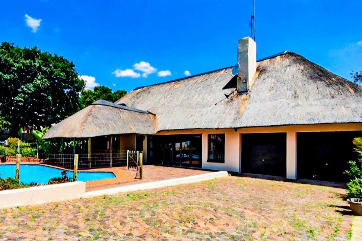 Rear view of a property featuring a traditional thatch roof, a swimming pool, and a paved driveway area.