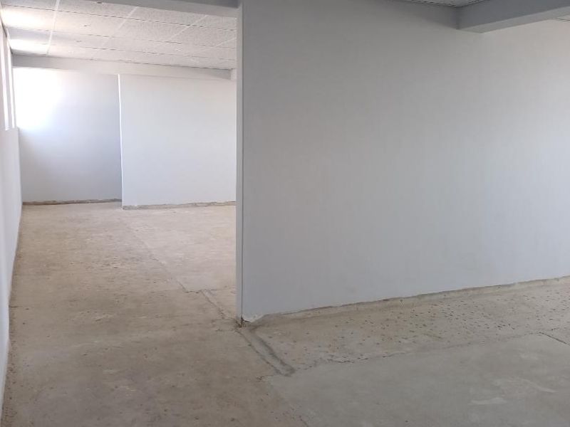 An open-plan retail or office space featuring neutral painted walls, an exposed ceiling grid, and unfinished concrete flooring ready for final finishes.
