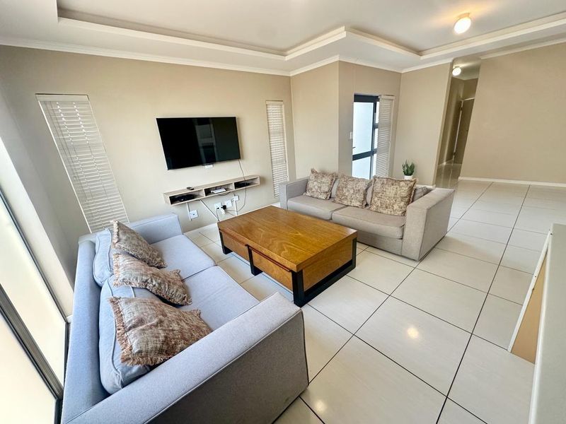 A bright and spacious living room featuring neutral walls, tiled flooring, recessed ceiling details, and a floating media shelf.